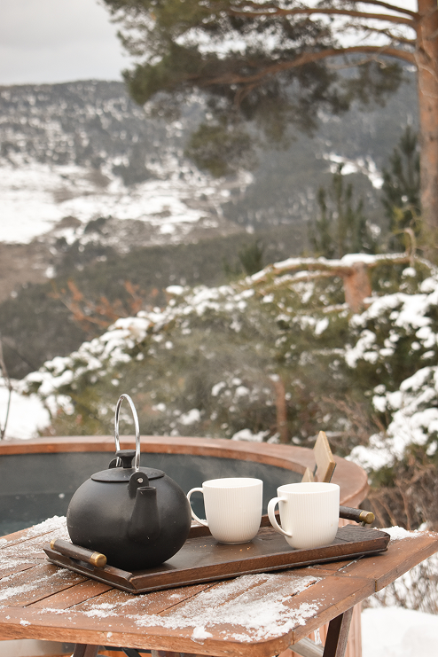 Théière noire et tasses blanches sur une table enneigée avec vue sur les montagnes à l'écolodge Minds and Mountains