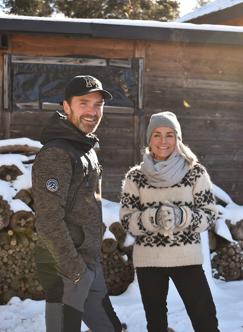 Couple smiling in winter clothes outside a wooden cabin at Minds and Mountains ecolodge