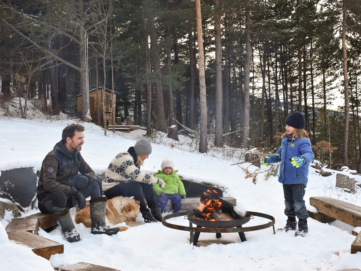Famille avec enfants et chien autour d'un feu de camp dans la neige à l'écolodge Minds and Mountains